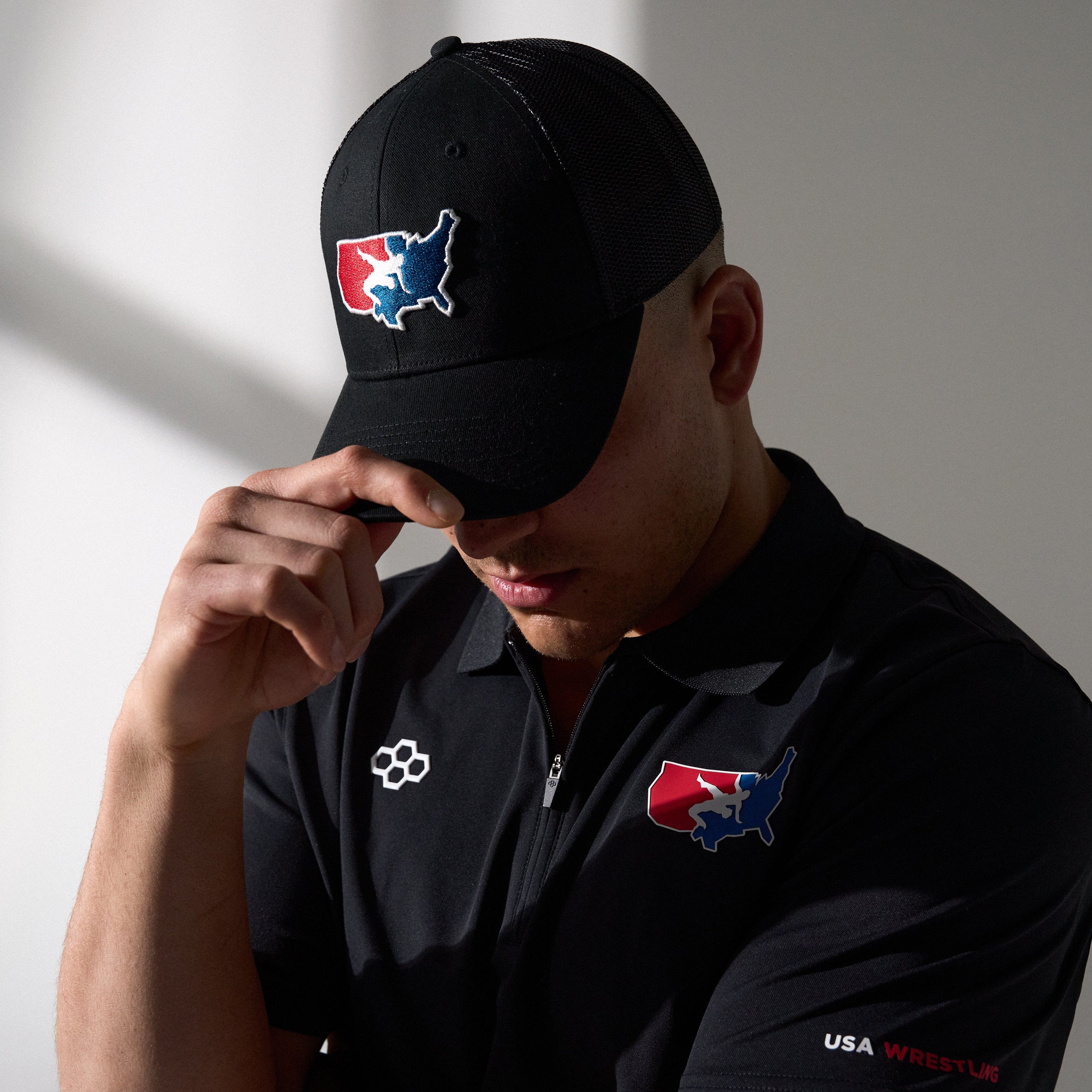 Man wearing a black USA Wrestling cap and matching polo shirt with logos against a neutral background