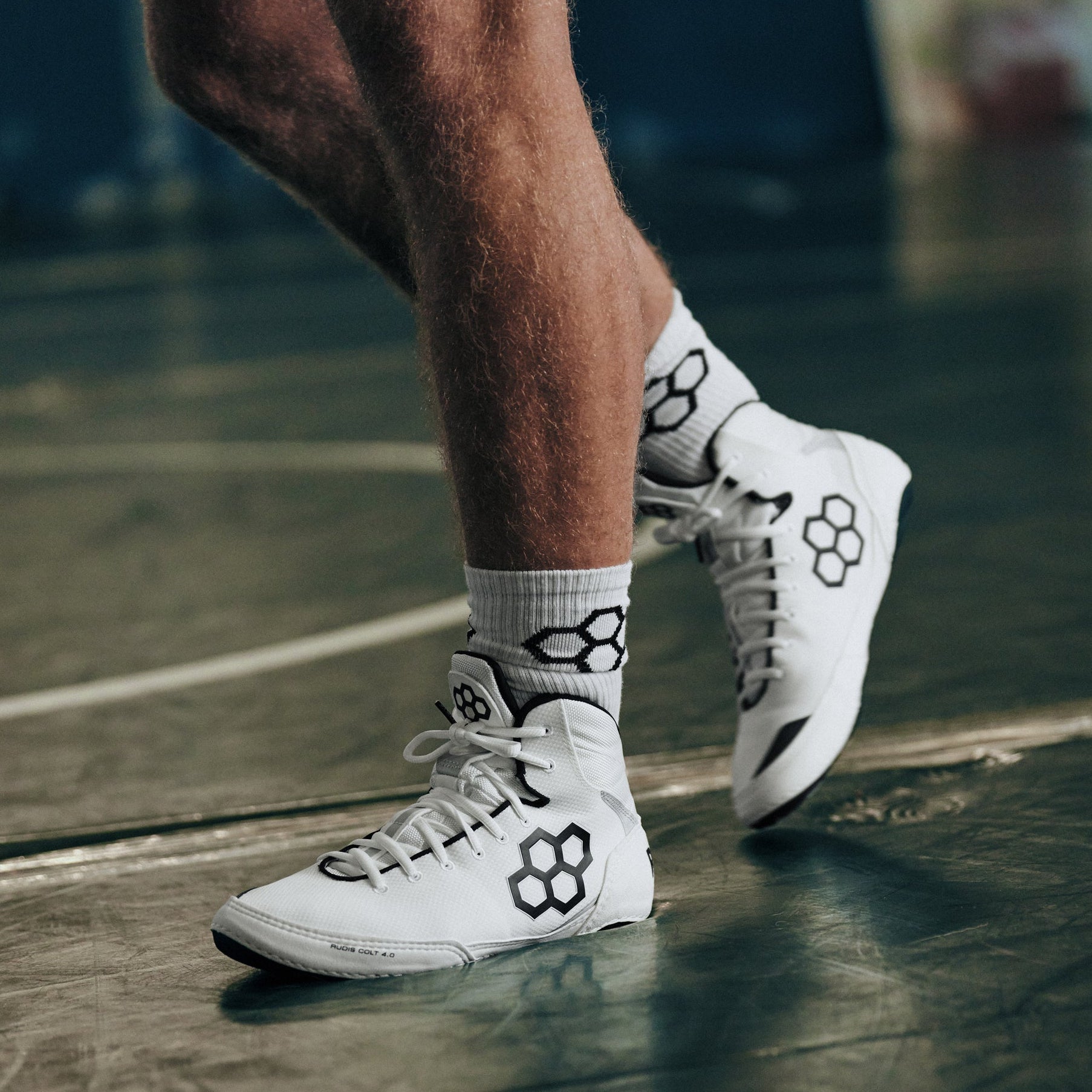 White Colt 4.0 Wrestling Shoes with black RUDIS Quadhex logo on a wrestling mat
