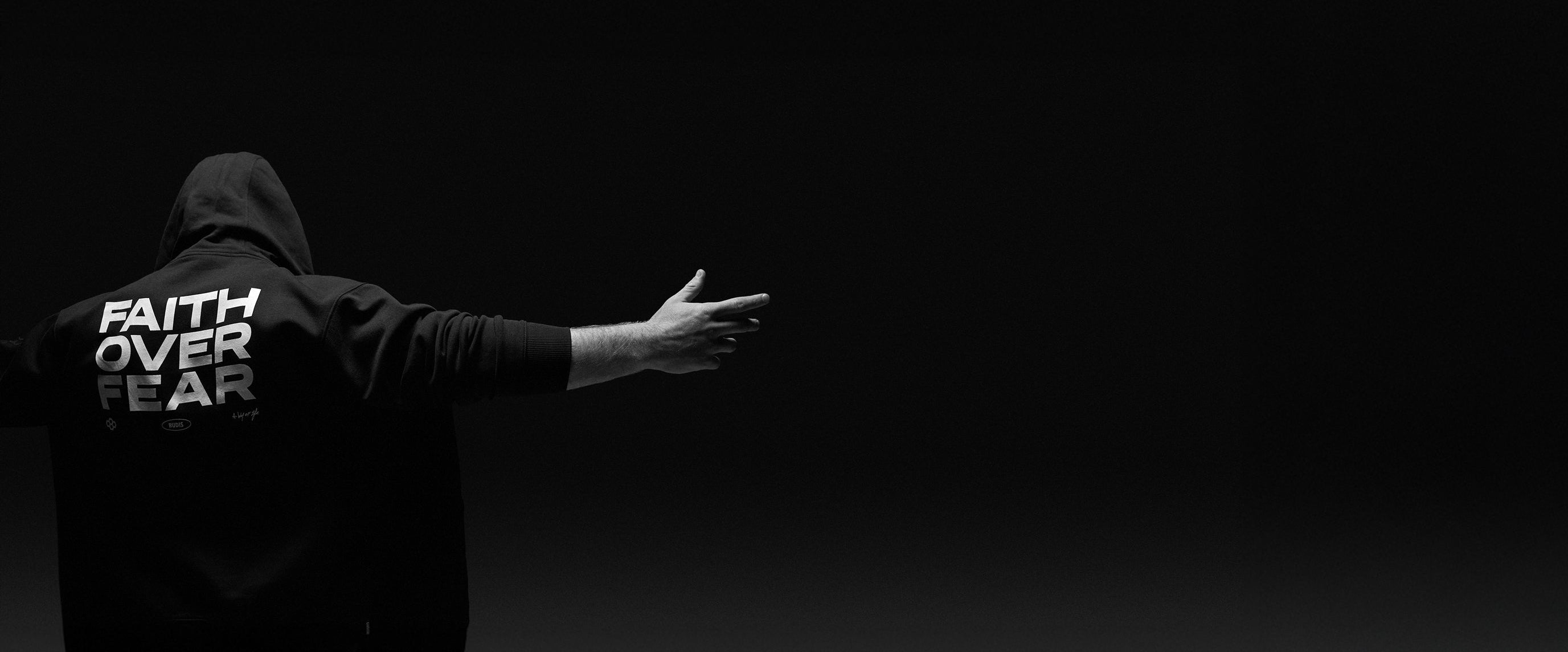 Person wearing a hoodie with 'Faith Over Fear' text on the back against a black background