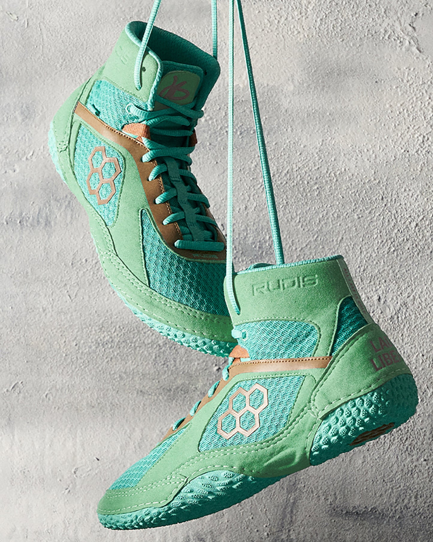 A pair of vibrant mint green wrestling shoes suspended by laces against a textured background showcasing a unique design with geometric accents