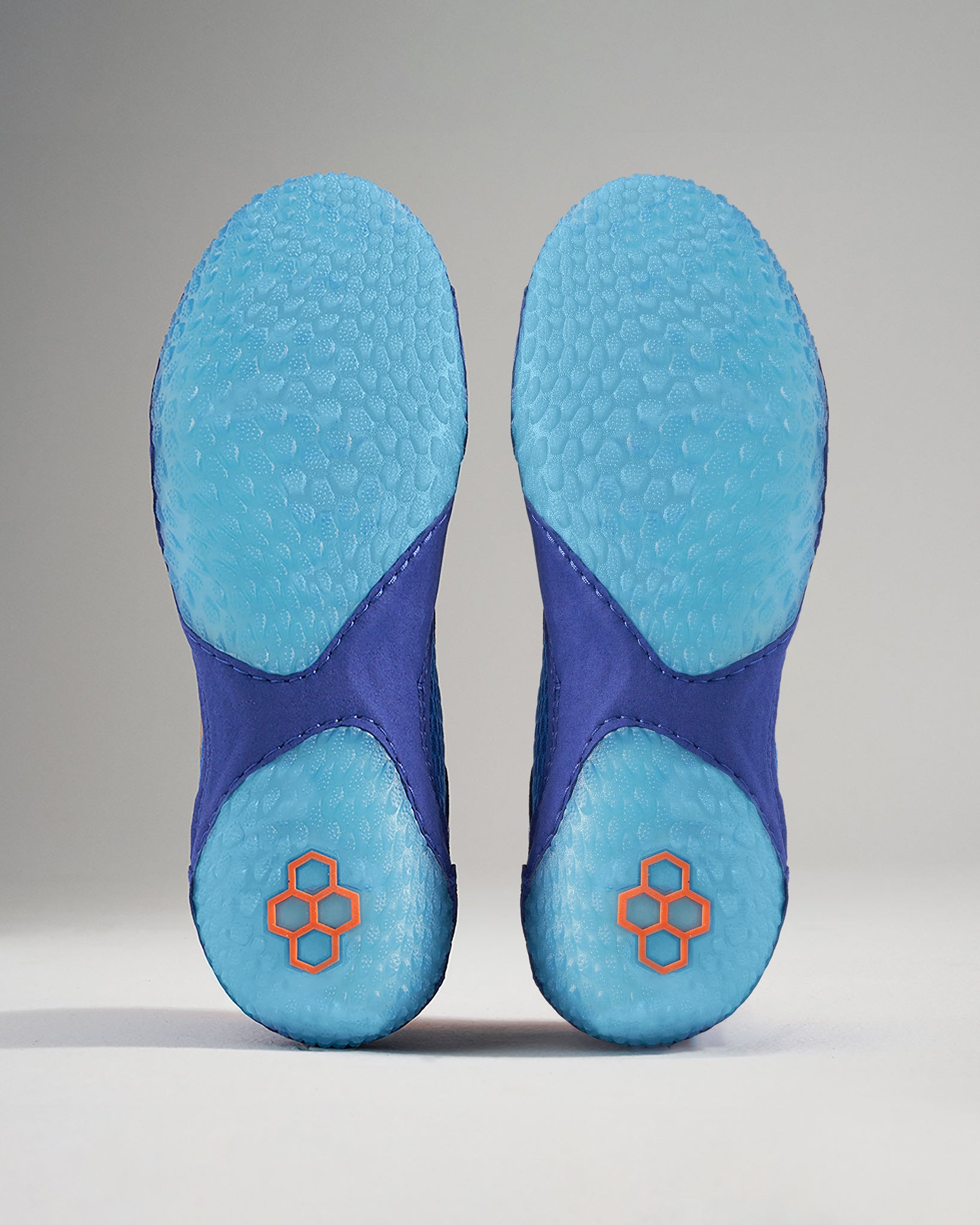 This image displays the soles of a pair of purple athletic shoes featuring a textured blue surface and unique geometric branding