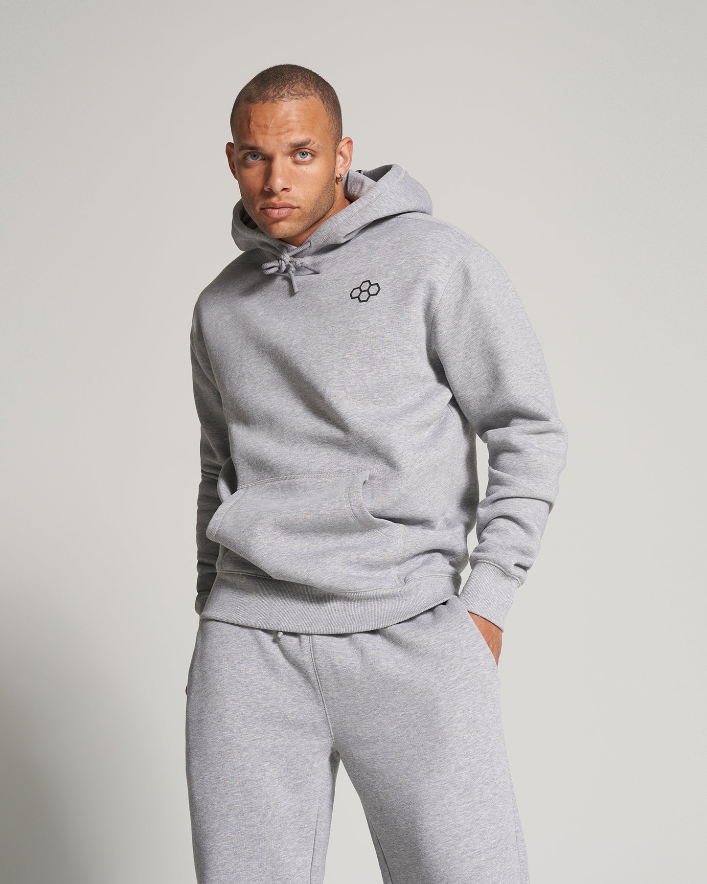 A stylish man poses confidently in a light gray hoodie and matching sweatpants showcasing a casual and contemporary fashion aesthetic