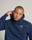 A man wearing a navy blue hoodie with a logo on the chest showcasing a casual style complemented by a serious expression and a visible scar on his forehead