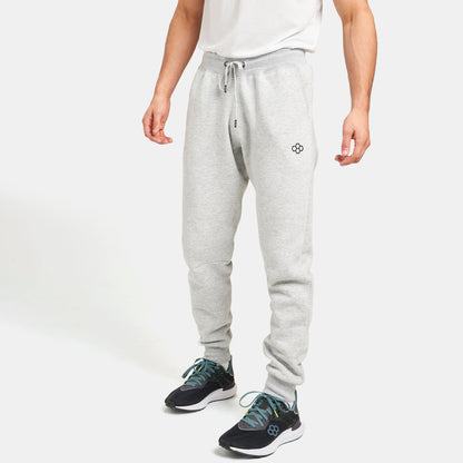 A man stands in a casual outfit featuring light gray sweatpants and black athletic shoes with teal accents