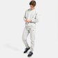 A young man dressed in a light gray athletic sweatshirt and matching sweatpants standing confidently with his hands on his wrists complemented by black sneakers featuring turquoise laces