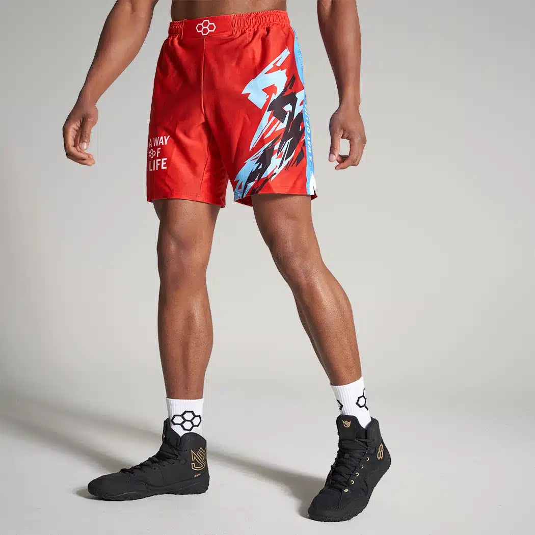 A male model showcases vibrant red athletic shorts featuring dynamic blue and black graphics paired with stylish black sneakers and patterned socks