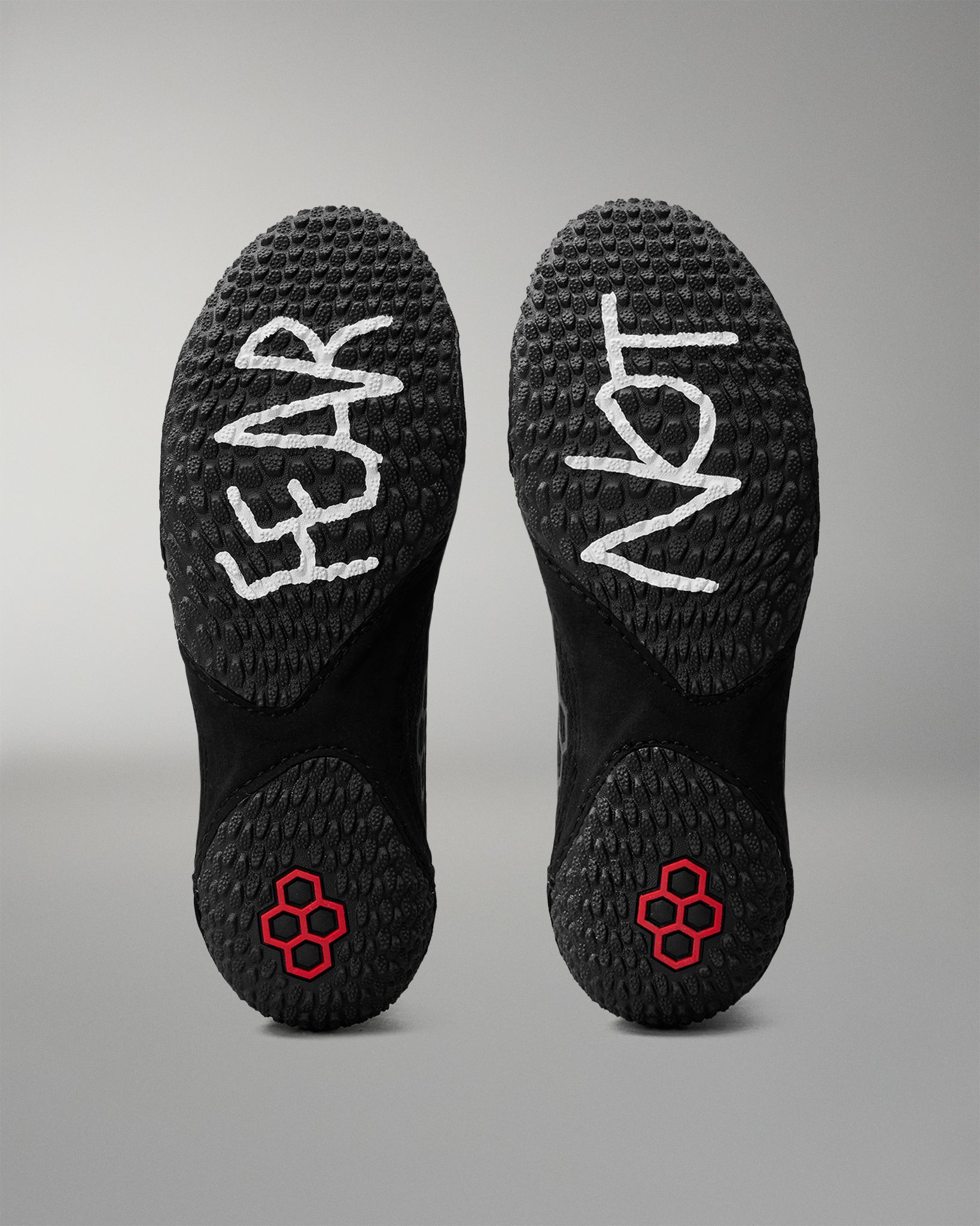 Black wrestling shoes with 'FEAR' and 'NOT' written on the soles against a gray background