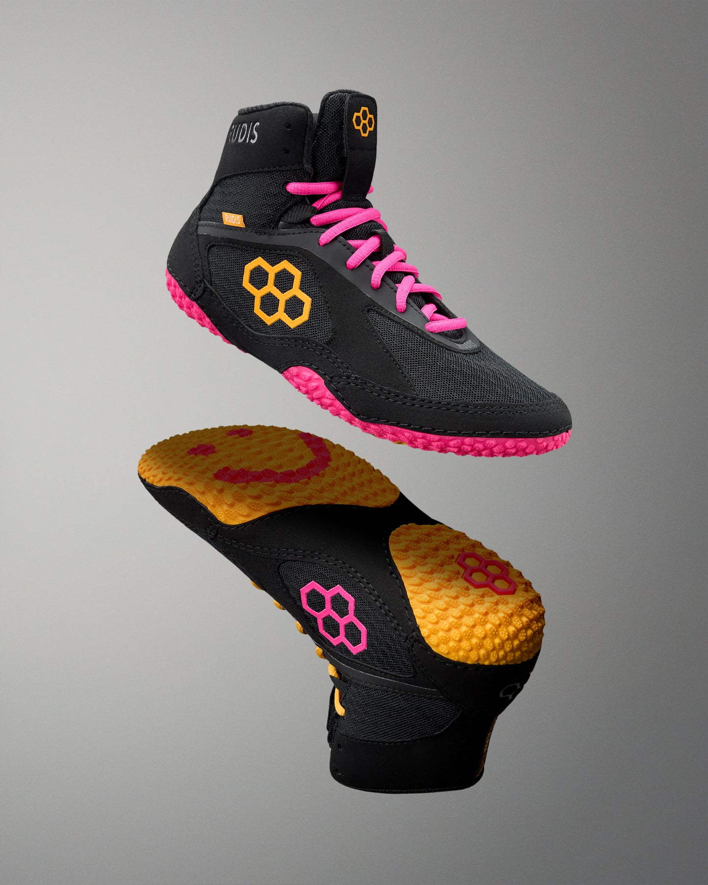 Black wrestling shoes with pink laces and yellow sole on a gray background