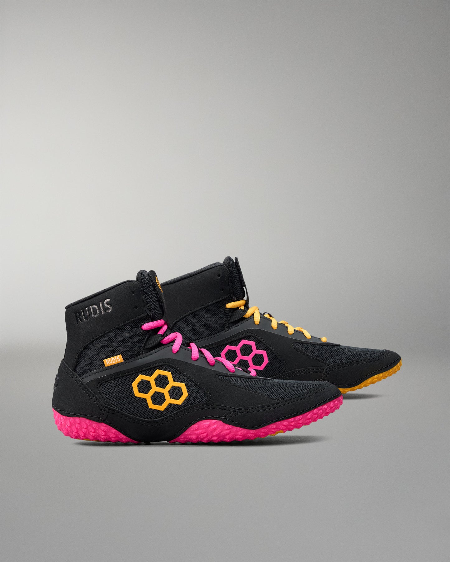 Black wrestling shoes with pink soles and yellow accents on a gray background