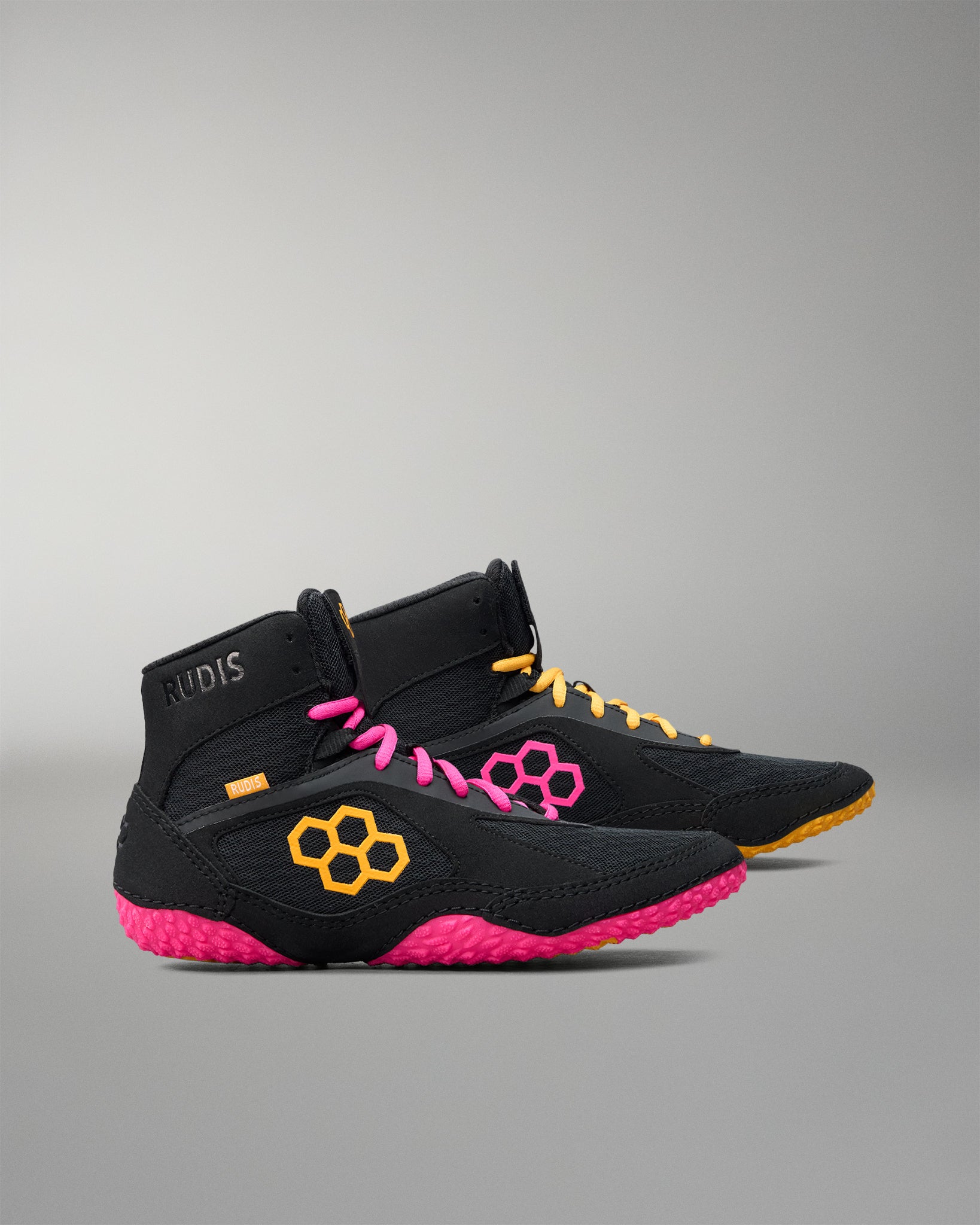 Black wrestling shoes with pink soles and yellow accents on a gray background