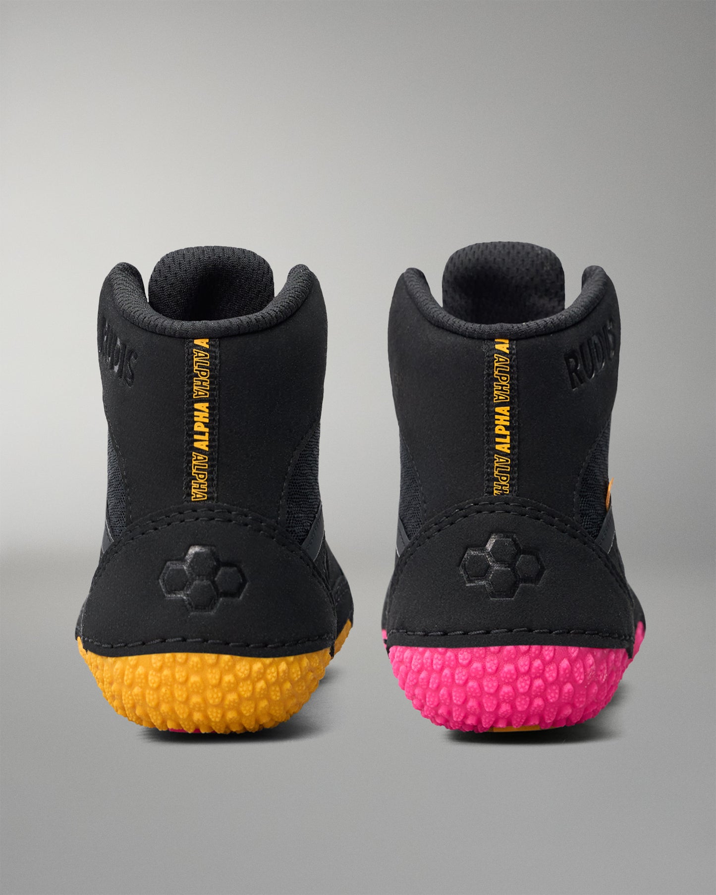 Black wrestling shoes with yellow sole and pink sole on a gray background