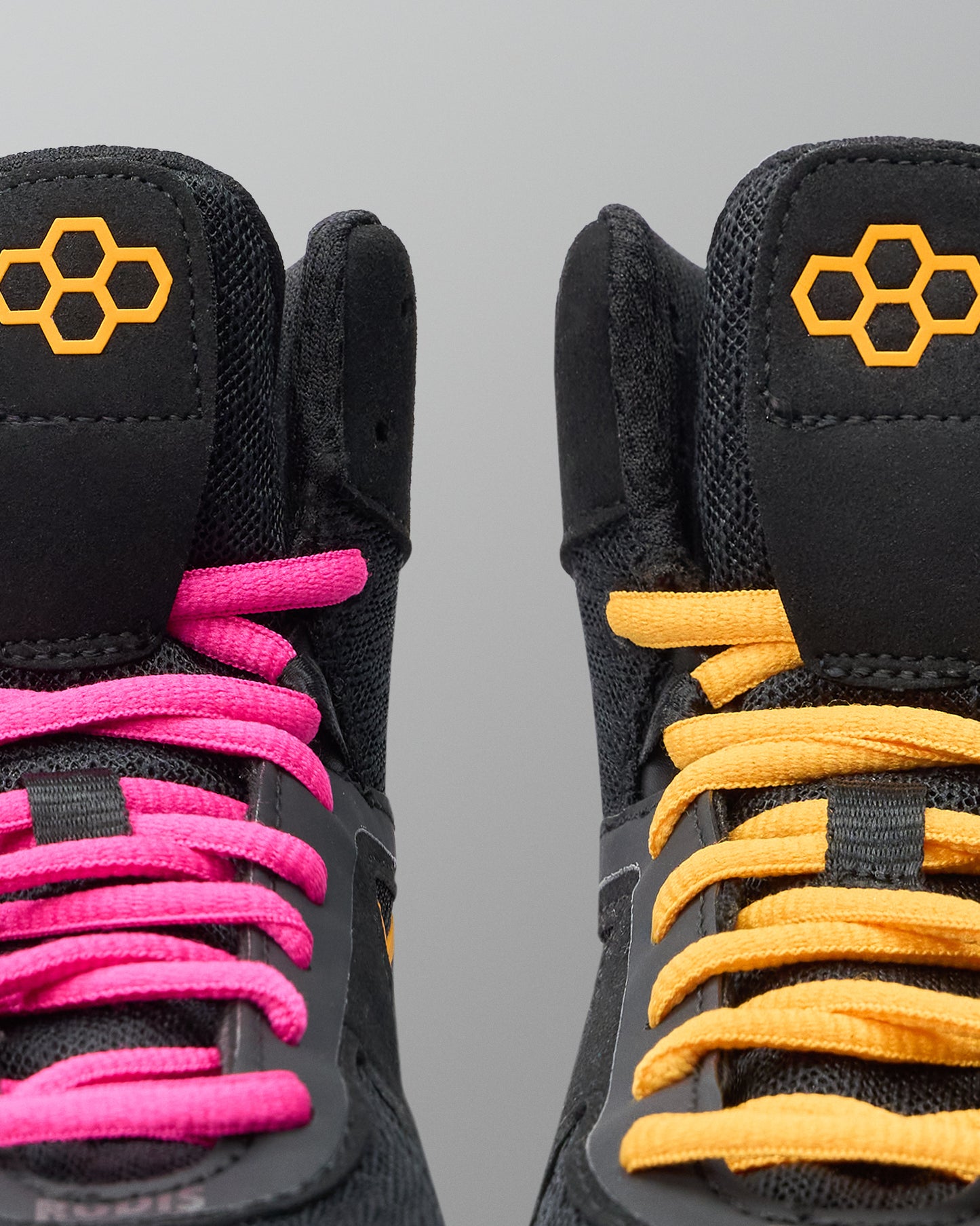 Black wrestling shoes with pink and yellow laces on a gray background
