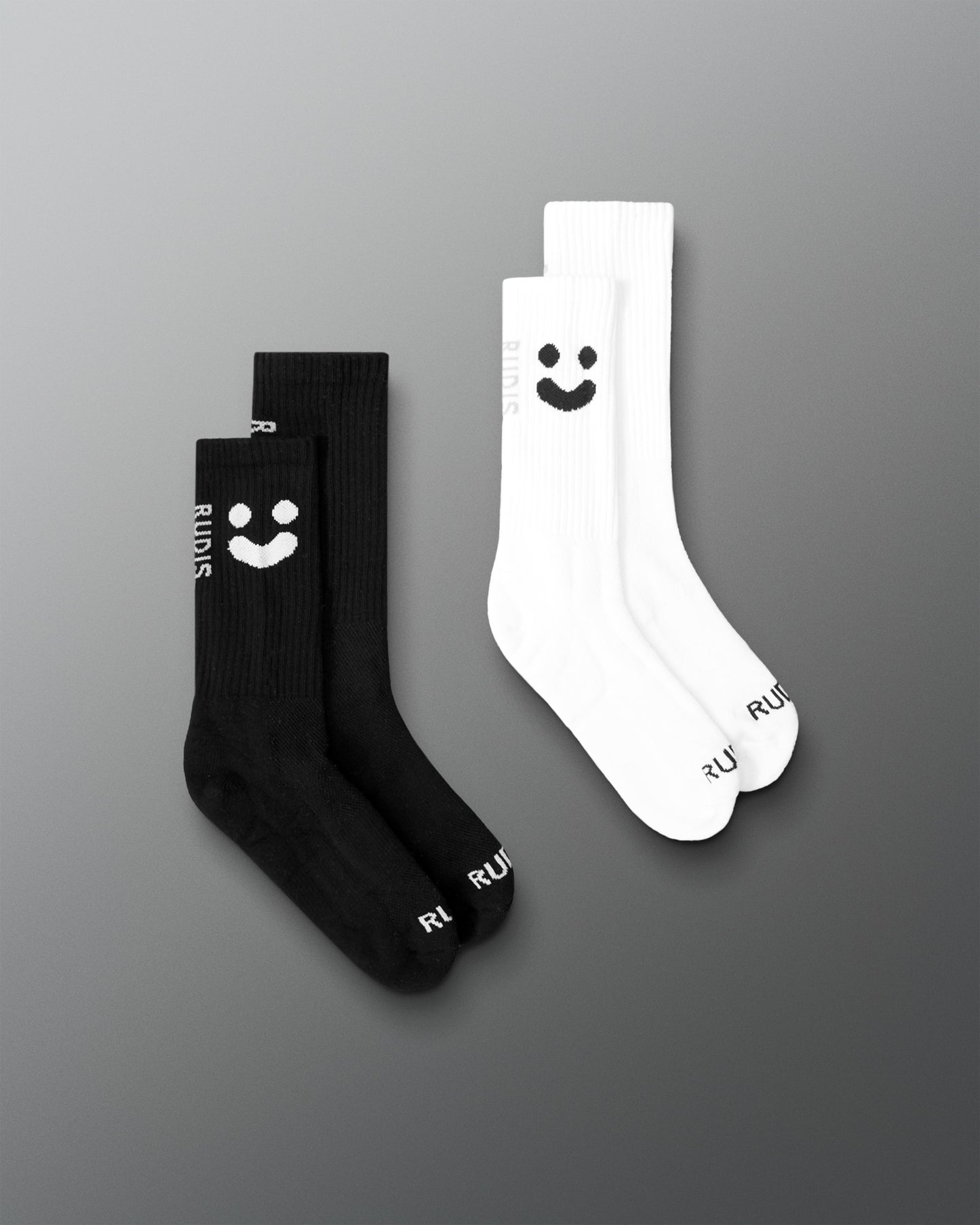 Two pairs of socks, two black and two white with a smiley face, on a gray background.