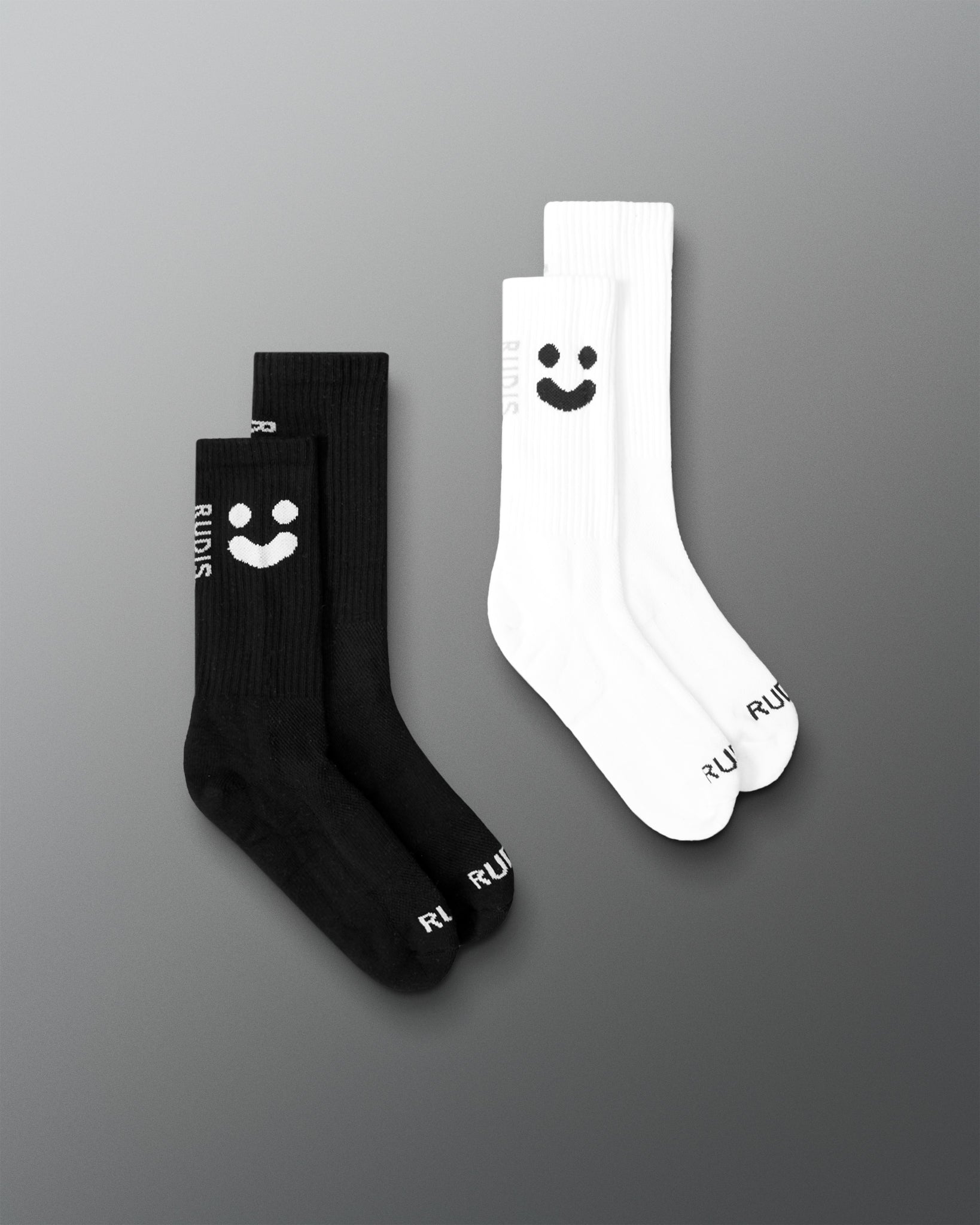 Two pairs of socks, two black and two white with a smiley face, on a gray background.