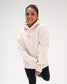 Female model wearing the RUDIS Love This Sport fleece hoodie in Bone, showing pink chest lettering, a relaxed fit, drawstring hood and sleeve graphics.