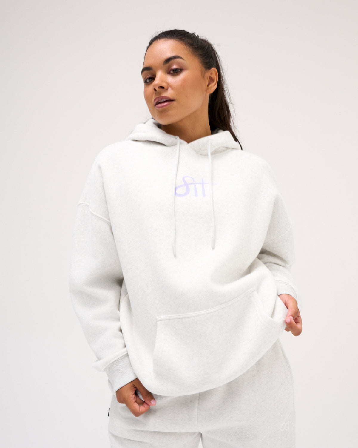Female model wearing the RUDIS Love This Sport fleece hoodie in Heather Silver, showcasing lavender chest lettering, relaxed shoulders and a kangaroo pocket.