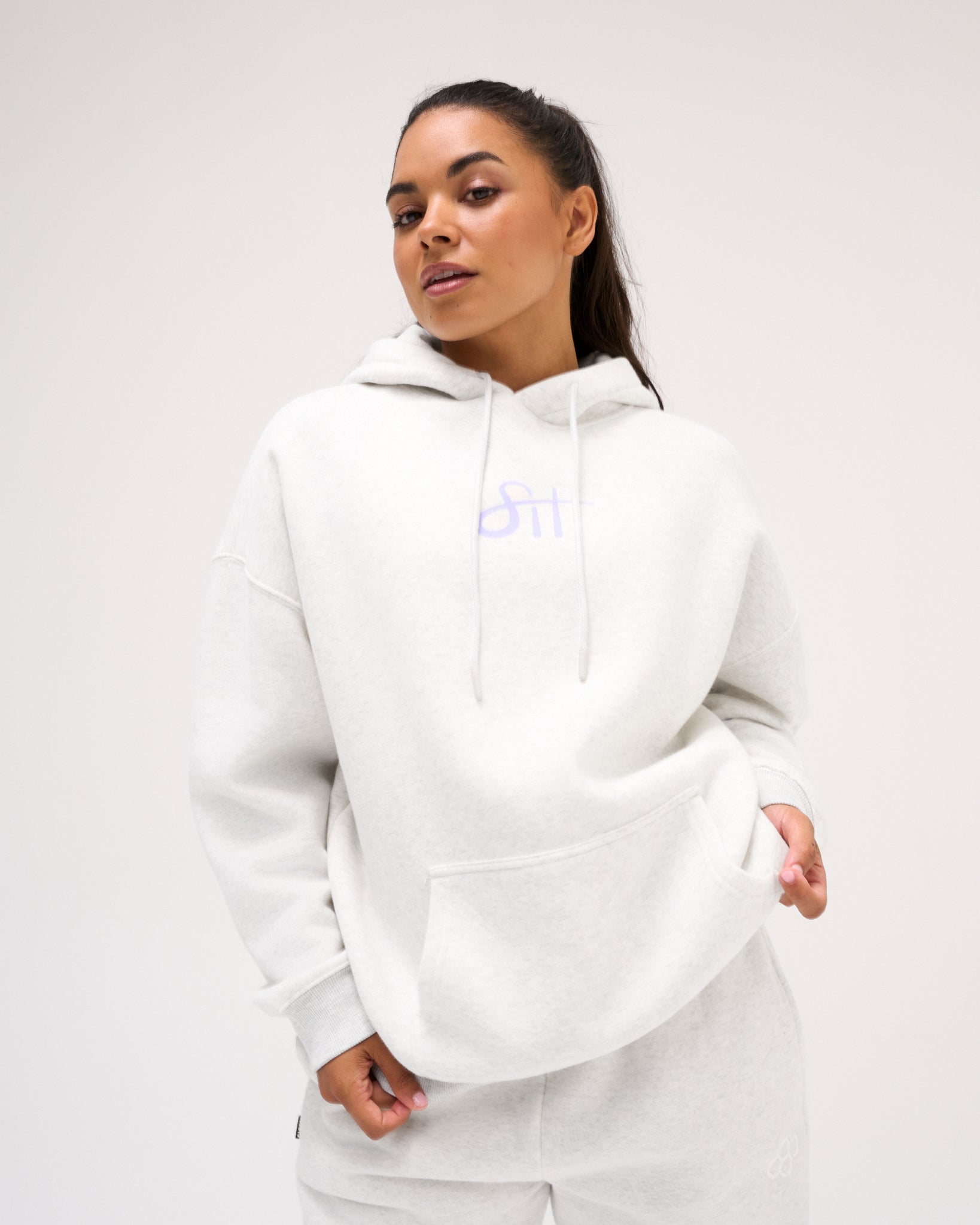 Female model wearing the RUDIS Love This Sport fleece hoodie in Heather Silver, showcasing lavender chest lettering, relaxed shoulders and a kangaroo pocket.