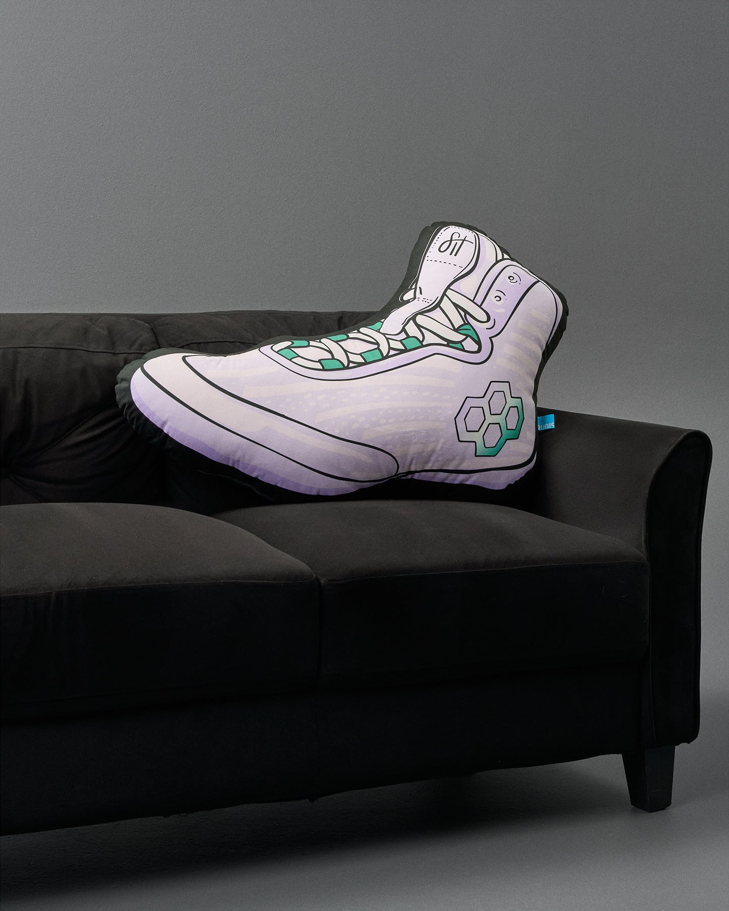Sneaker-shaped pillow on a black couch against a gray background