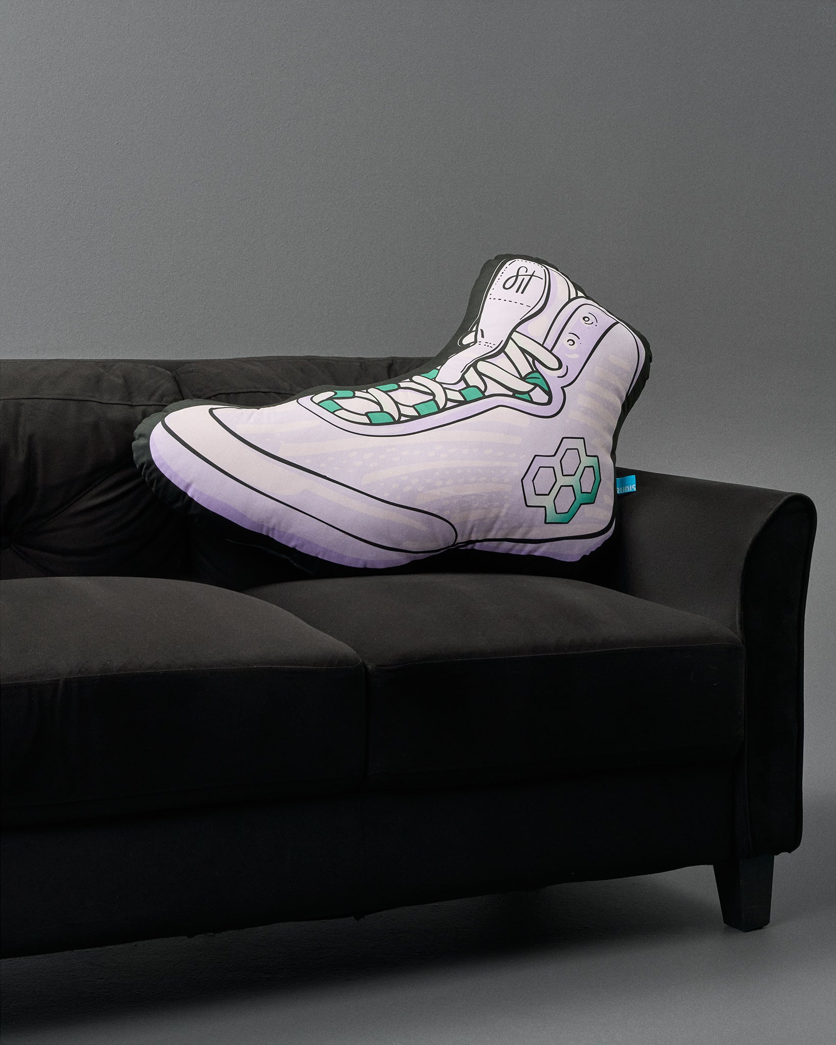 Sneaker-shaped pillow on a black couch against a gray background