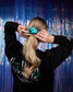 Person tying a teal scrunchie in their blonde hair against a colorful curtain background