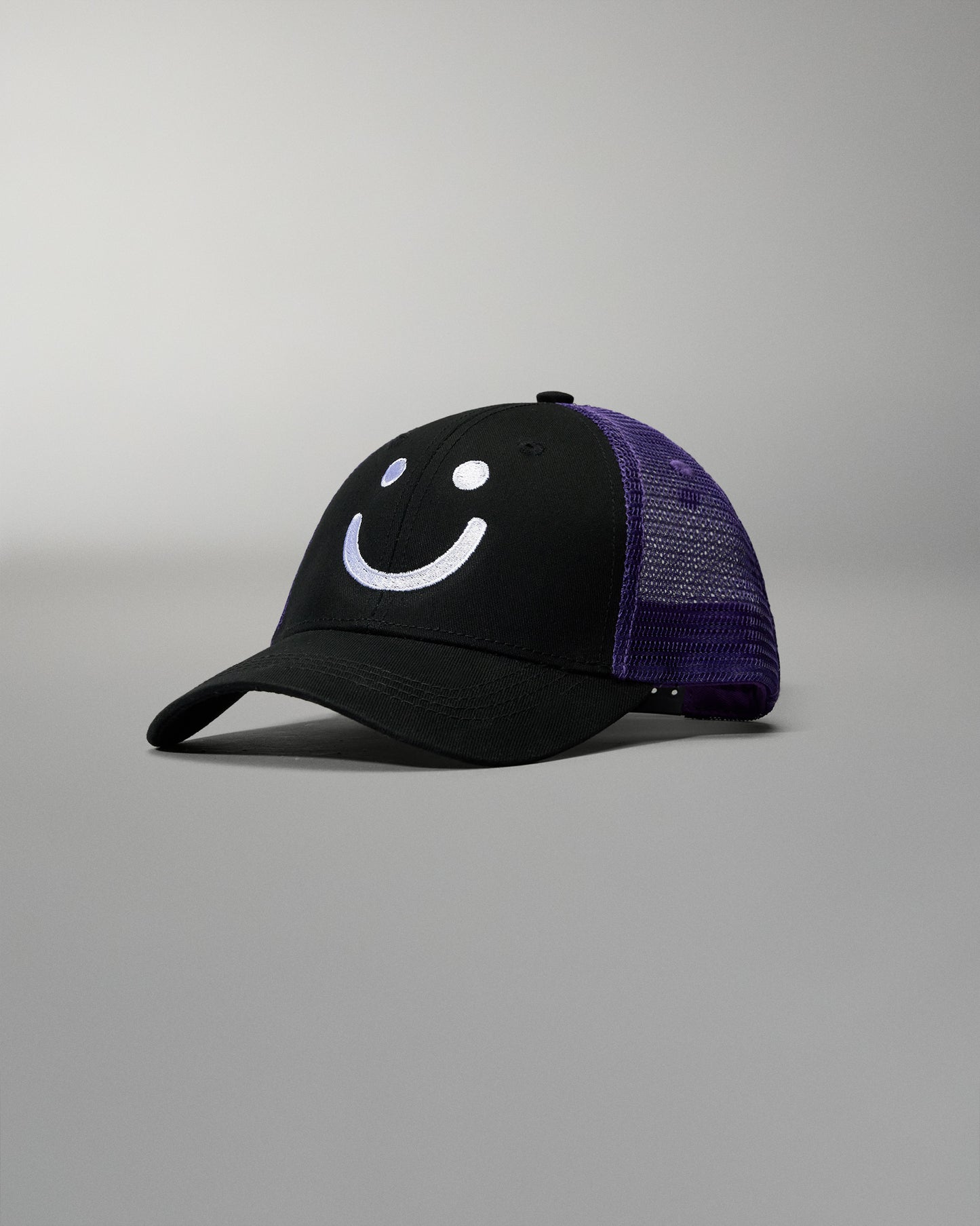 Black cap with purple mesh back and smiley face design on a gray background