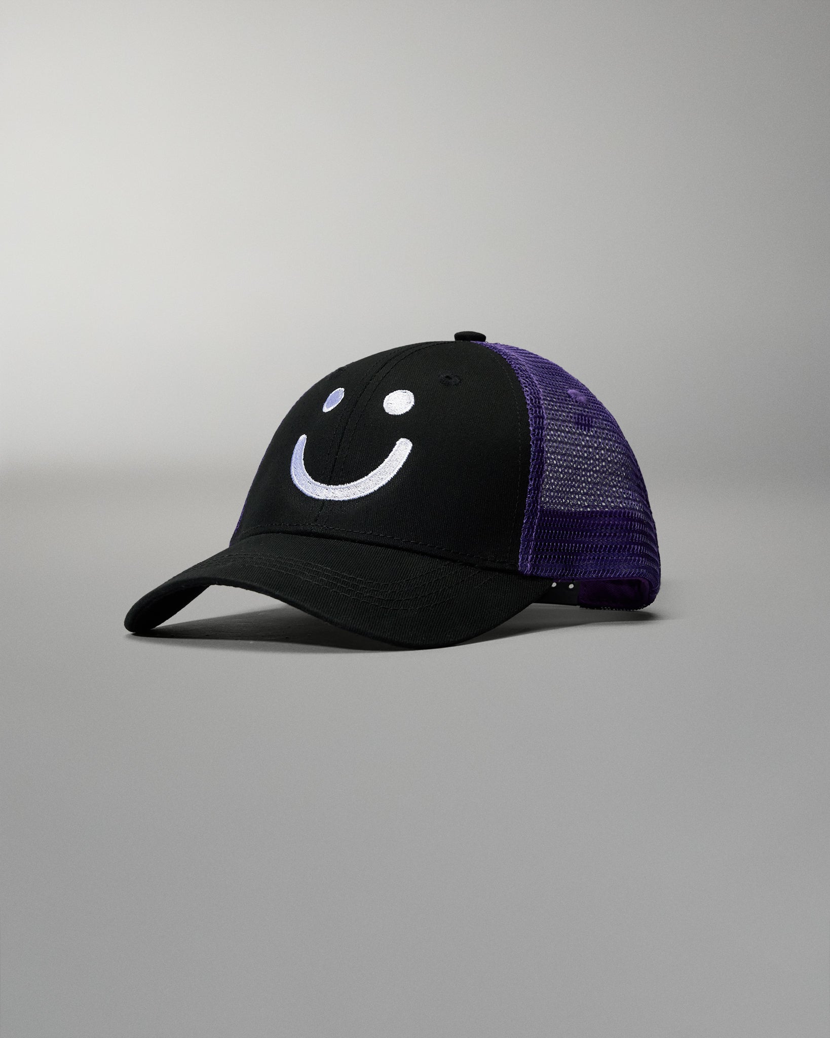 Black cap with purple mesh back and smiley face design on a gray background