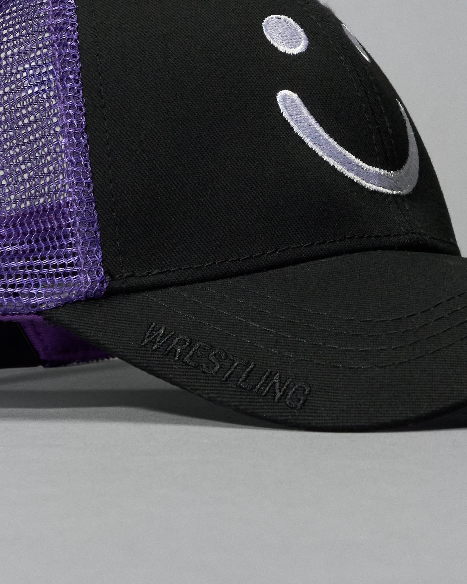 Black and purple cap with smiley face design on a gray background
