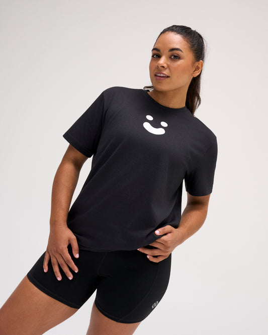 Woman wearing the RUDIS SH Smile Elite Super Soft T-Shirt in black with a white smile graphic, paired with black athletic shorts.