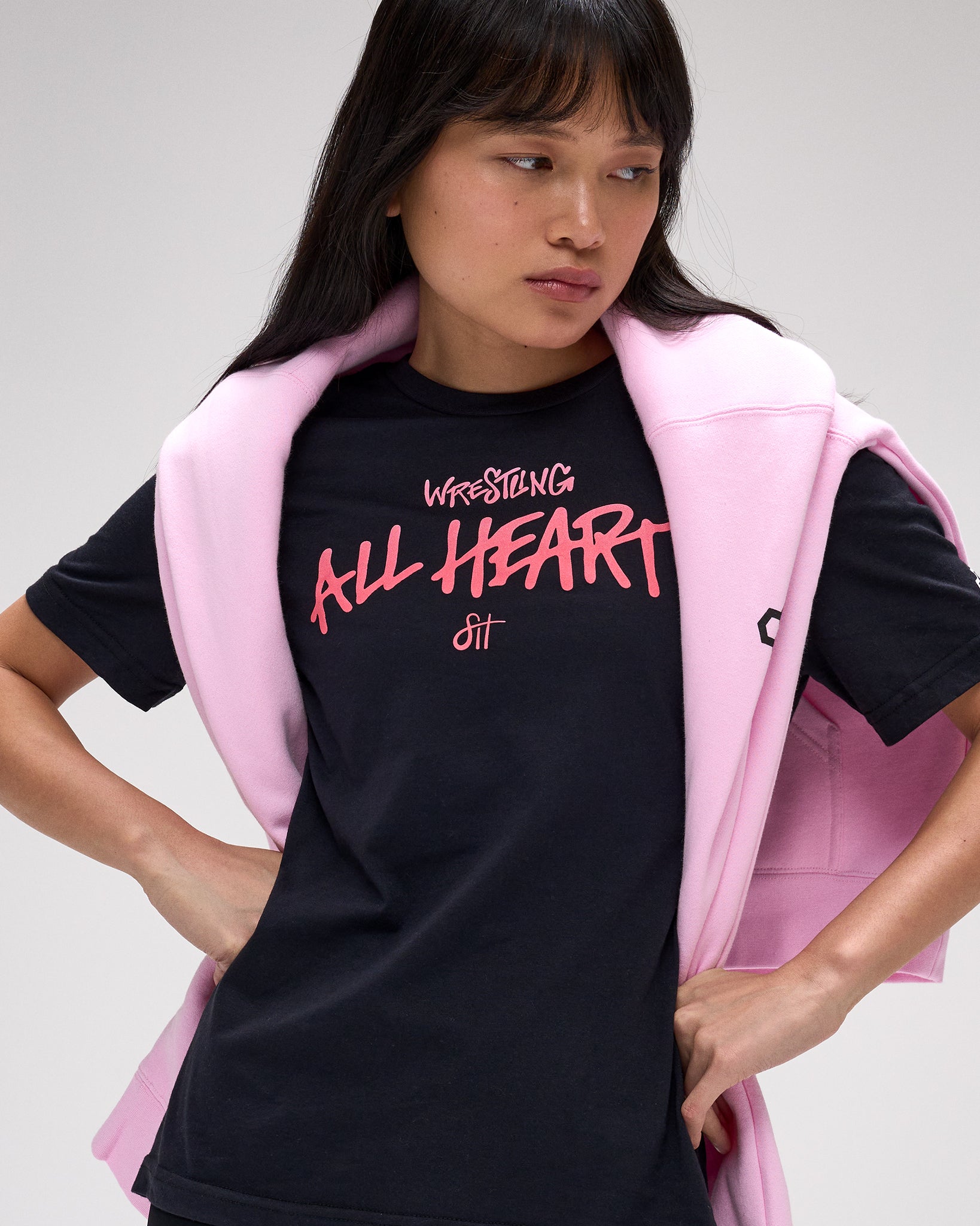 Person wearing a black t-shirt with pink text and a pink crewneck on a white background