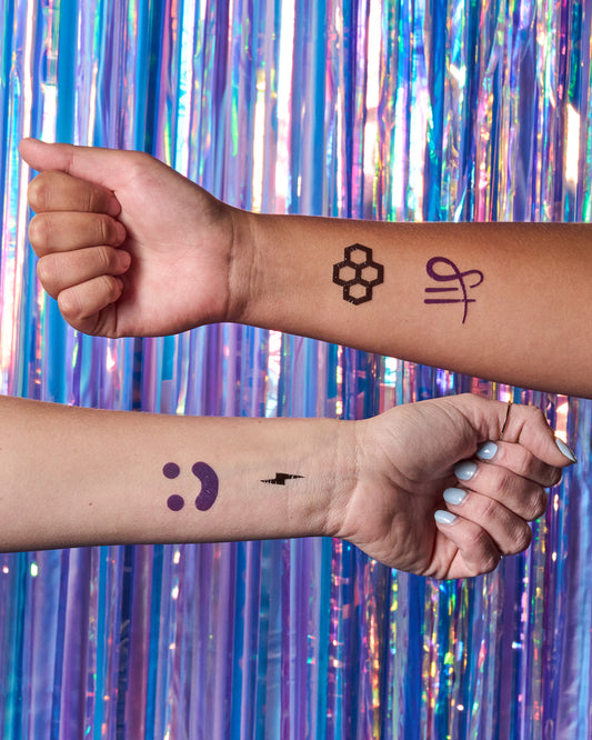 Two arms with temporary tattoos against a colorful, metallic curtain background