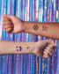 Two arms with temporary tattoos against a colorful, metallic curtain background