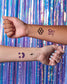Two arms with temporary tattoos against a colorful, metallic curtain background
