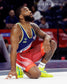 A male wrestler in a blue and red uniform kneels on a mat looking upwards with a focused expression during the 2024 Team Trials event