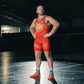 A muscular wrestler in a vibrant red uniform stands confidently on a wrestling mat showcasing his strong physique and determination