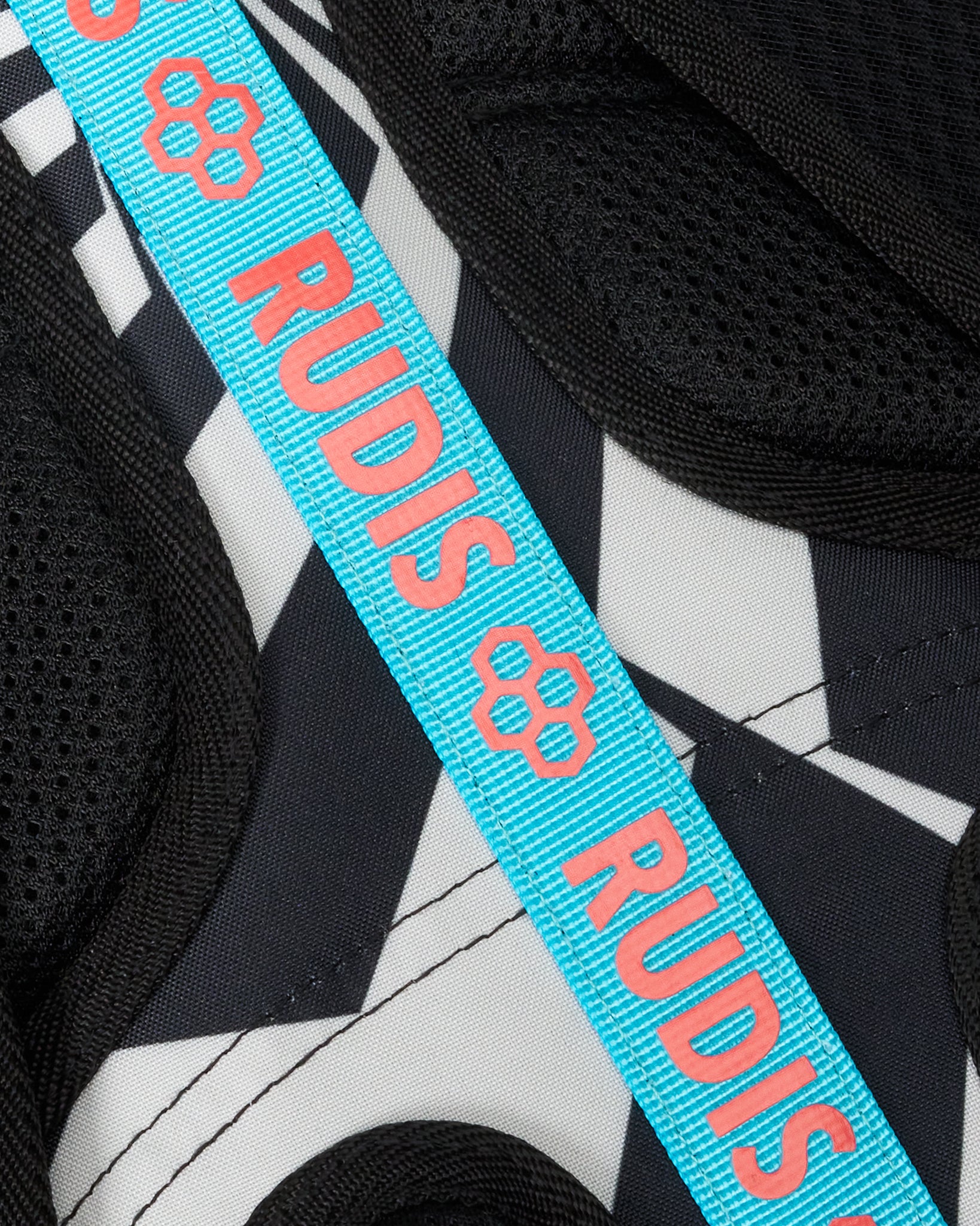 Close-up of a black, white, and gray patterned shoe with a bright turquoise strap featuring the brand name 'RUDIS' in coral pink.