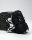 A black backpack with white logo details and a white-and-black wrestling shoes draped over its side, set against a light gray studio background with a black foam wrestling mat.