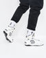 White and black high-top wrestling shoes with white crew socks featuring black text and a cross, worn with black pants against a white studio background.