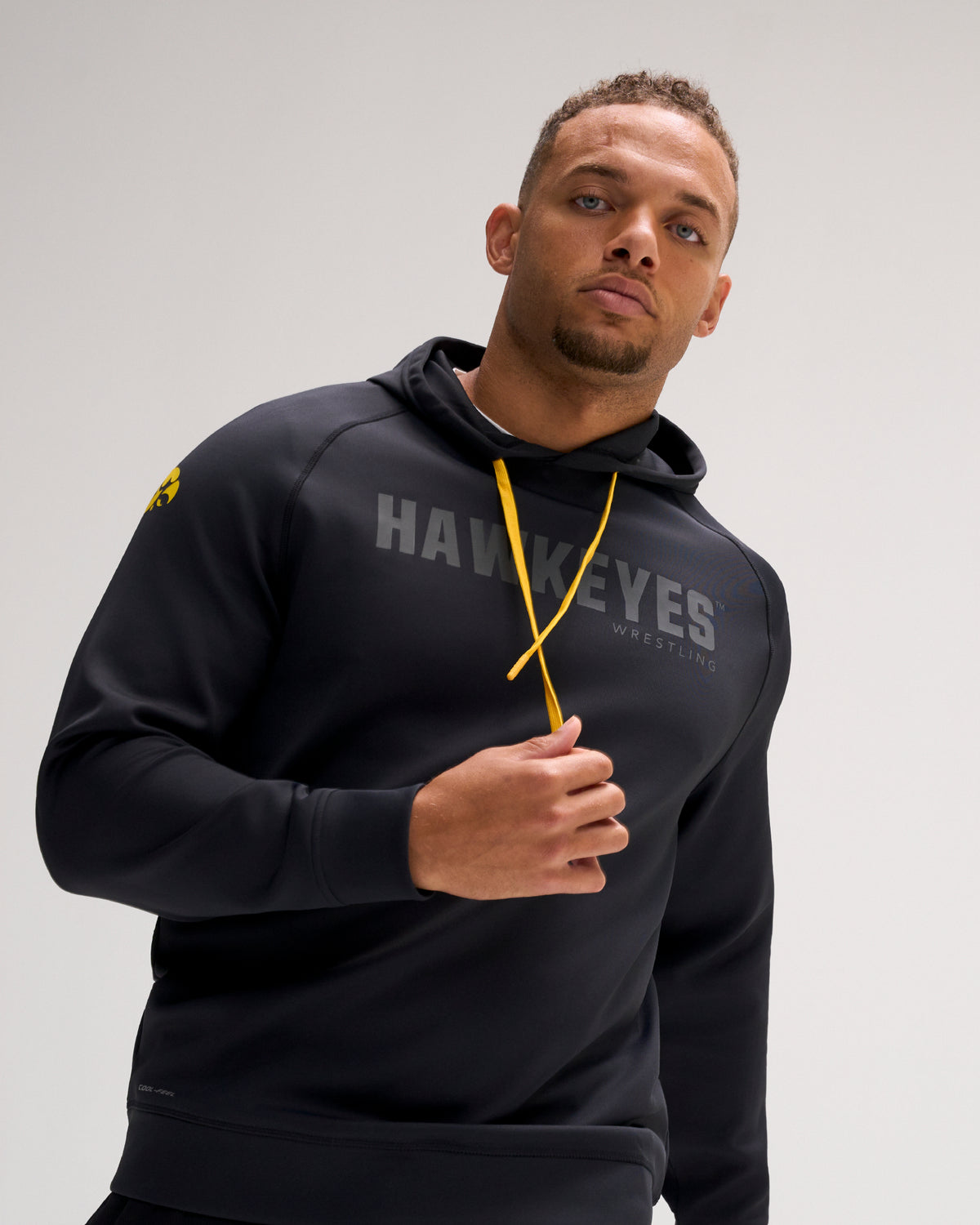 Model wearing the RUDIS Iowa Hawkeyes Cool Feel Hoodie in black with tonal Hawkeyes Wrestling chest graphic, gold drawcords, and Iowa logo on the sleeve.
