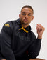 Model wearing the black RUDIS Iowa Hawkeyes Cool Feel Hoodie with tonal Hawkeyes Wrestling graphic, gold drawcords, and gold Iowa Hawkeyes sleeve logo.