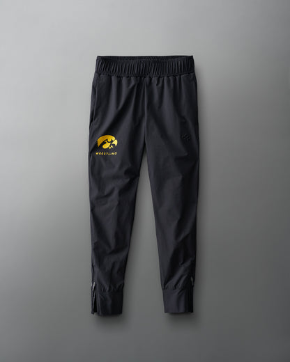 Youth athletic pants in black with a gold iowa hawkeyes wrestling logo on the left leg, laid flat on a grey background.