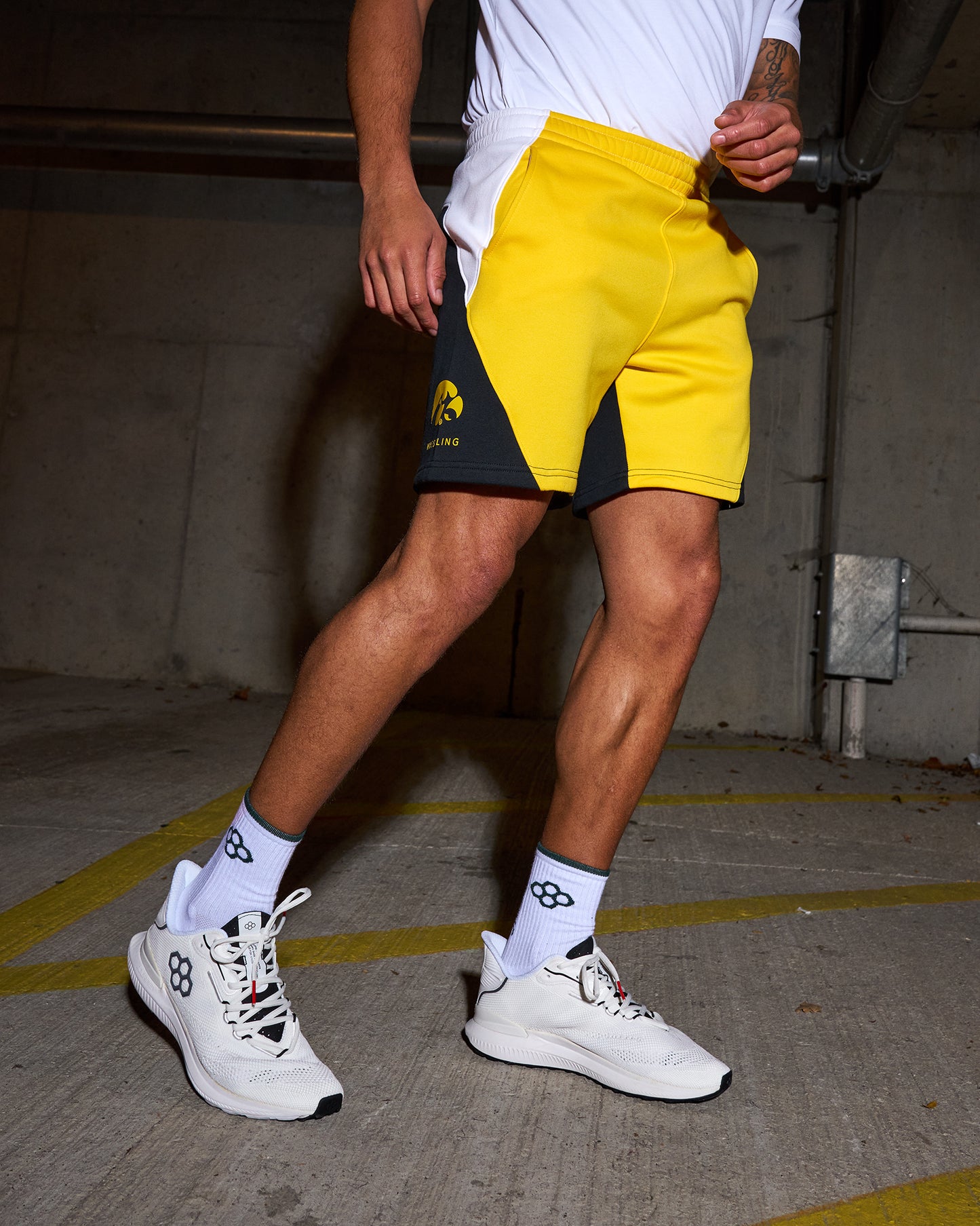 Person wearing yellow and black shorts with a logo, white sneakers, and socks in an urban setting.