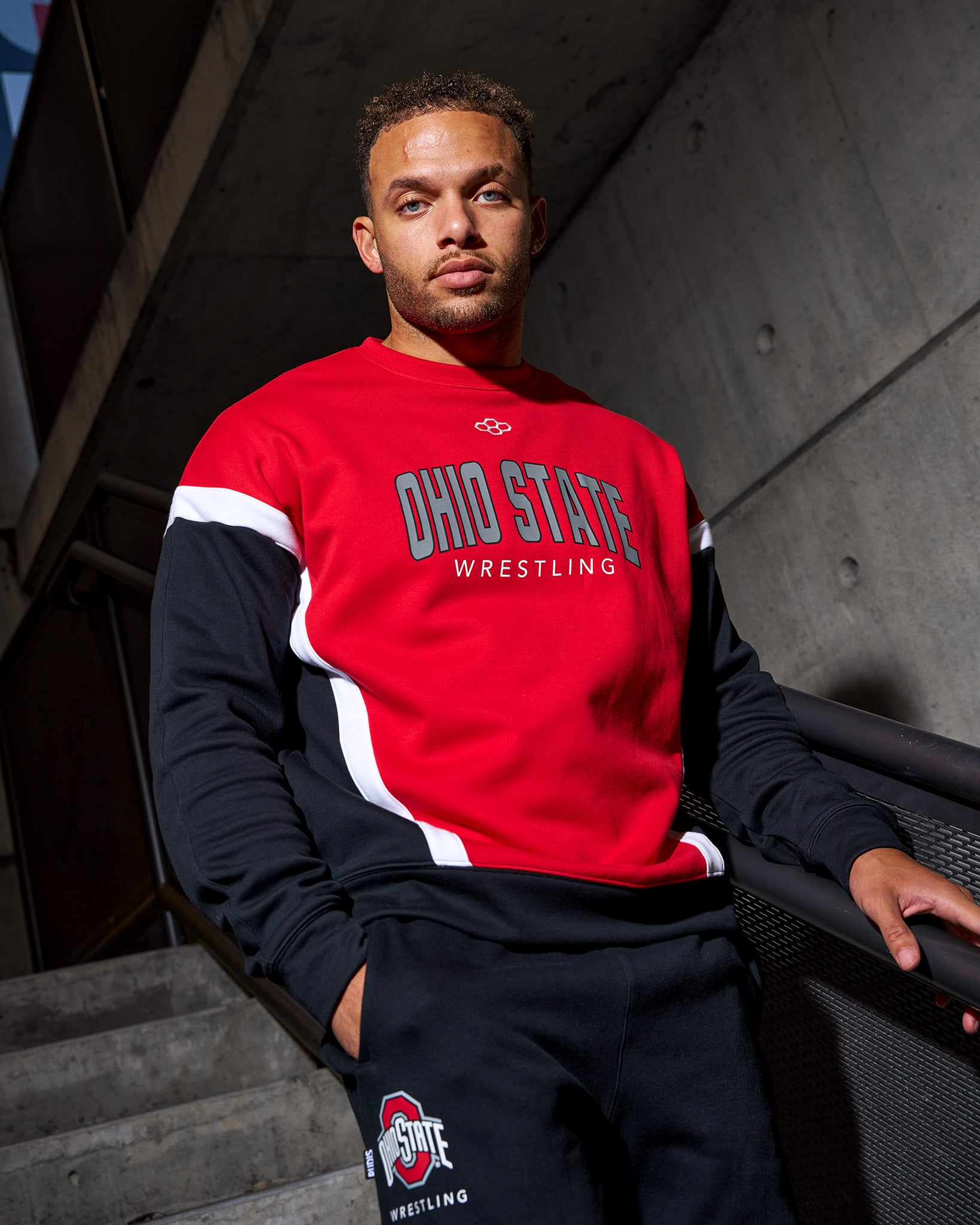 Person wearing a red and black Ohio State Wrestling sweatshirt sitting on steps.
