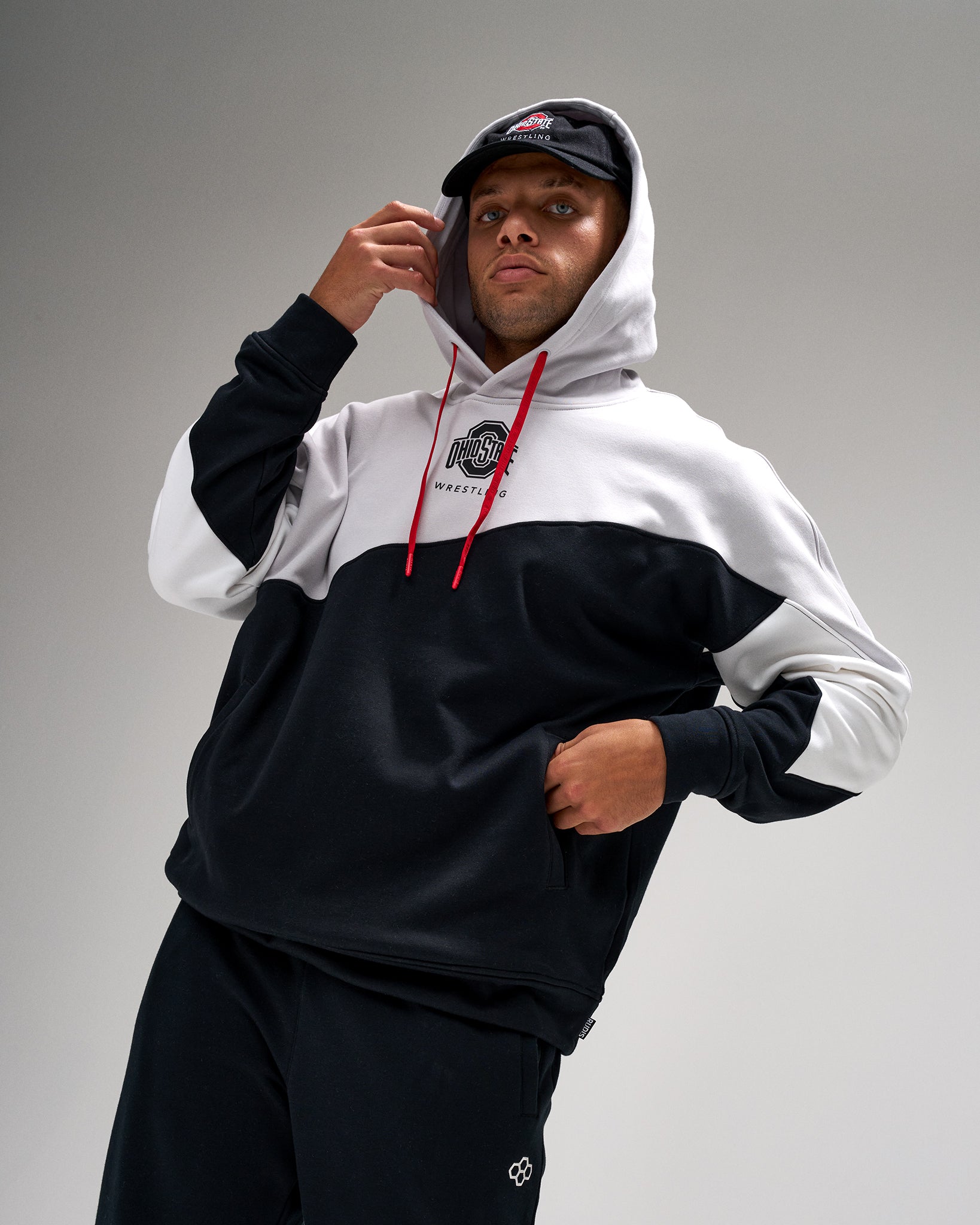 Person wearing a black and white hoodie with a logo, standing against a gray background