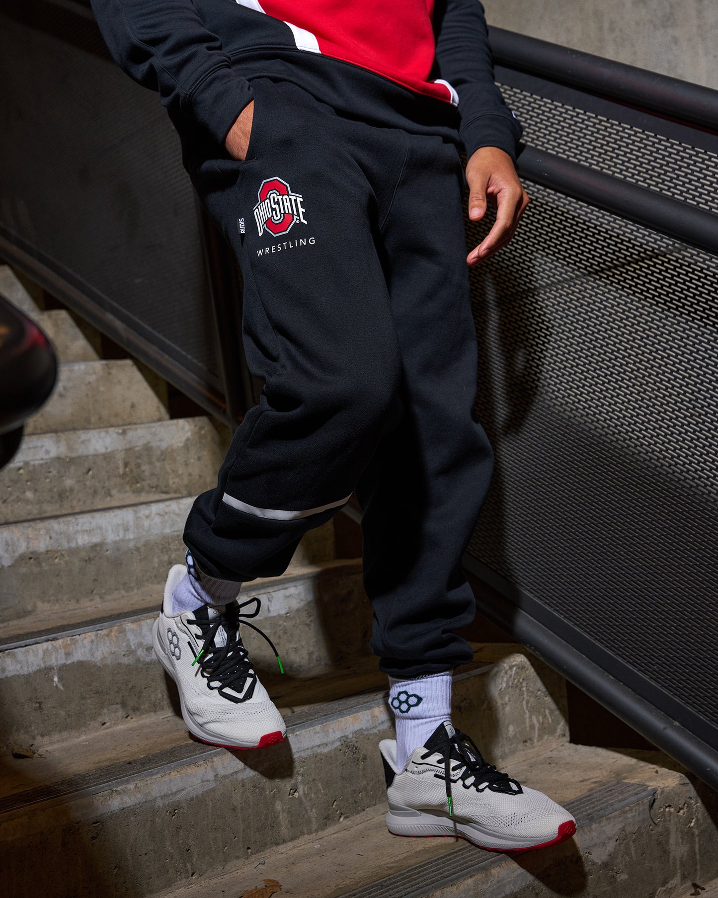Person wearing a black tracksuit with a wrestling logo, sitting on steps.