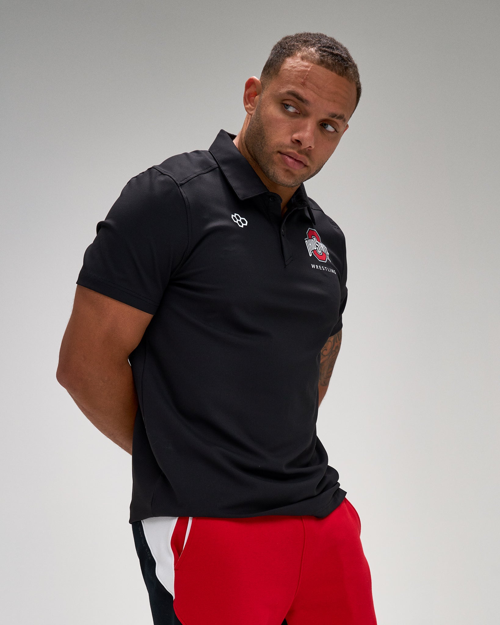 Man wearing a black polo shirt with a logo on a gray background