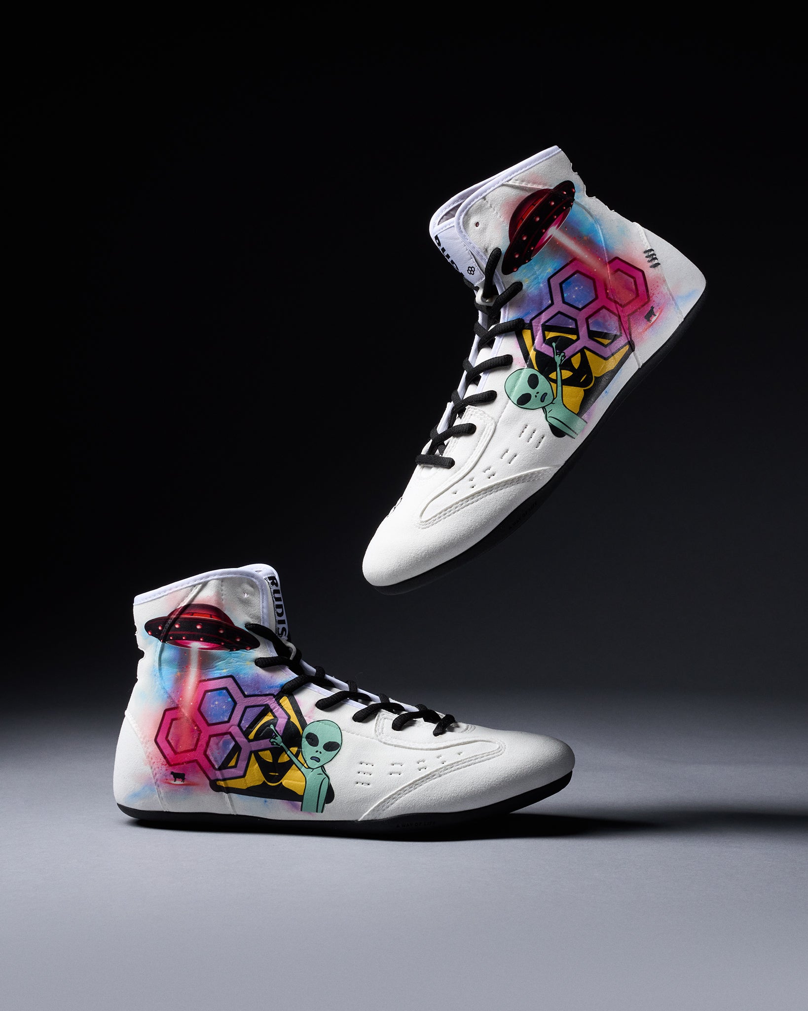 White wrestling shoes with colorful alien and geometric designs on a dark background