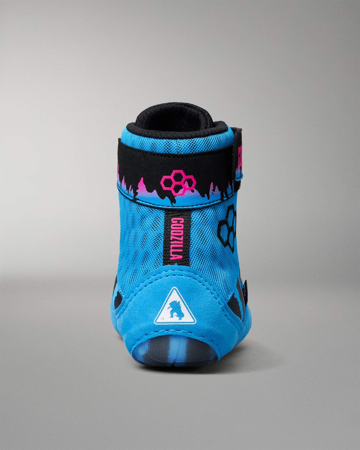 A single high-top wrestling shoe in bright blue with black, pink, and white graphics, including the brand name GODZILLA on a black strap and a white triangle logo on the toe area, photographed against a neutral gray background.