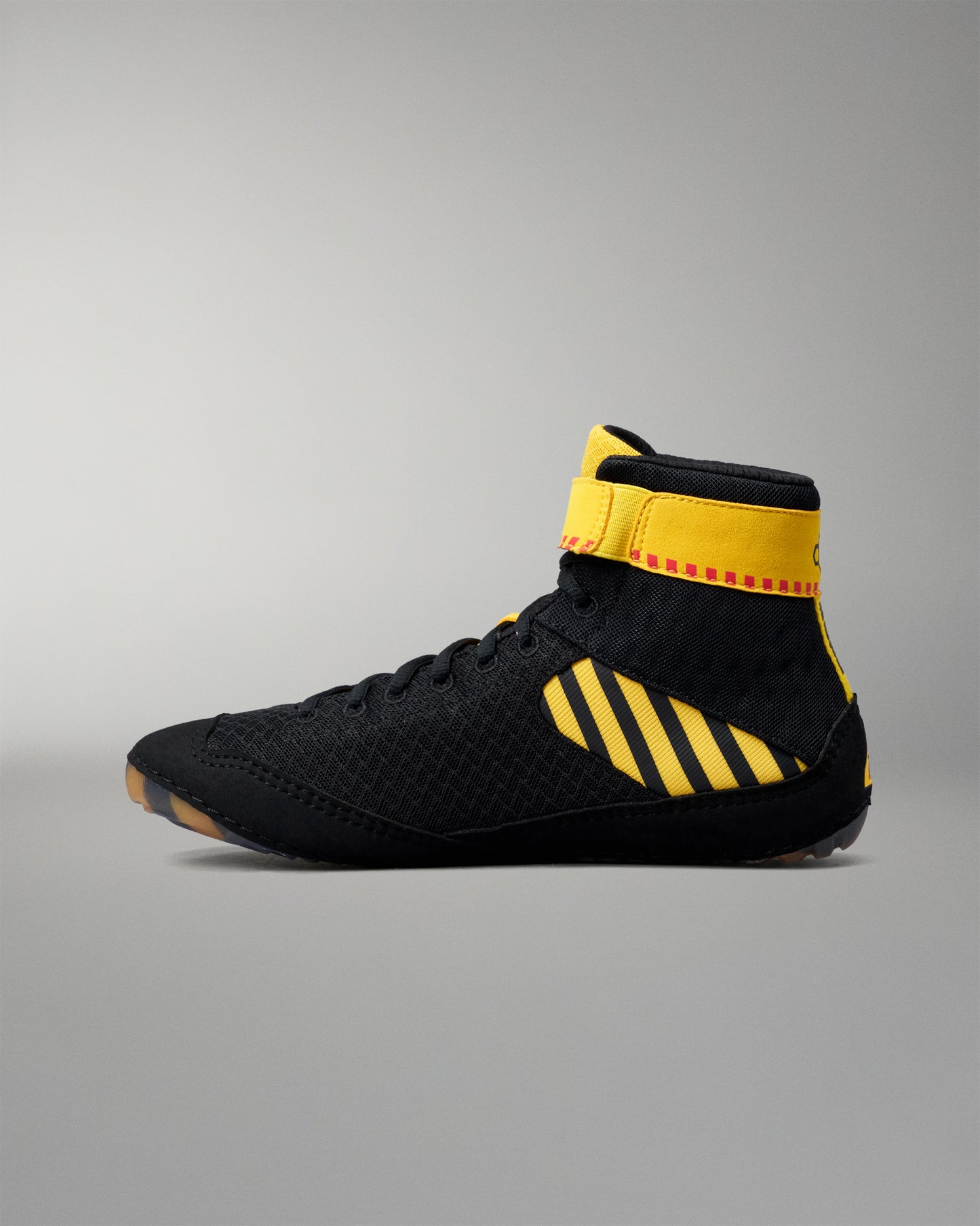 A high-top wrestling shoe in black with bold yellow stripes and a yellow ankle collar, shown in profile against a neutral gray background.