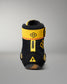 A single high-top wrestling shoe shown from the back on a neutral gray studio background. The shoe is primarily black with bold yellow accents, including a wide yellow strap around the ankle, a vertical yellow tab, and yellow graphic details.