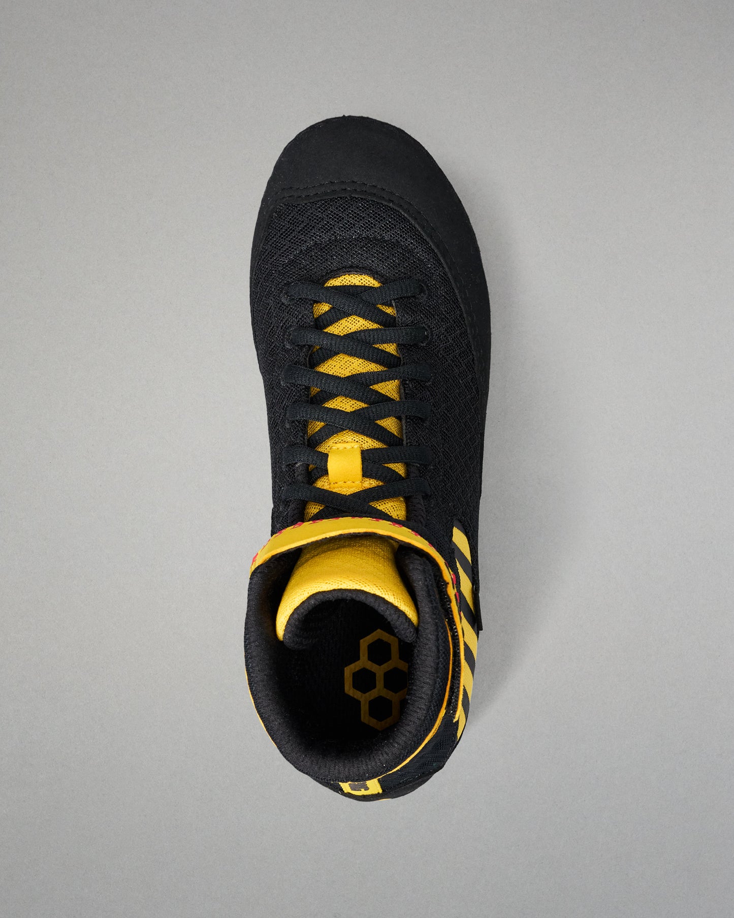 A black high-top wrestling shoe with bright yellow accents on the laces, collar, and heel, shown from a top-down view on a neutral gray background.